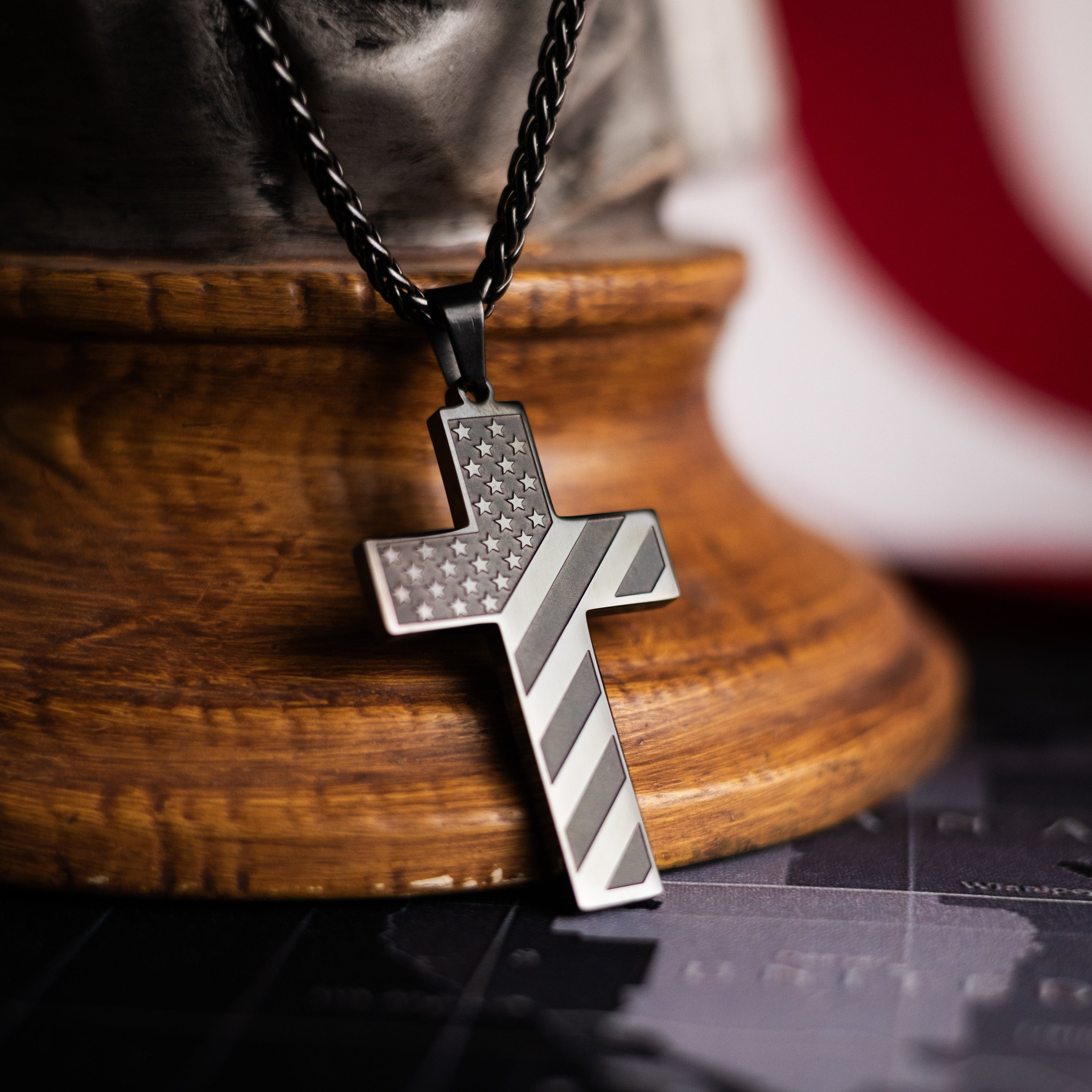 Silver cross pendant on a wooden stand with an American flag in the background