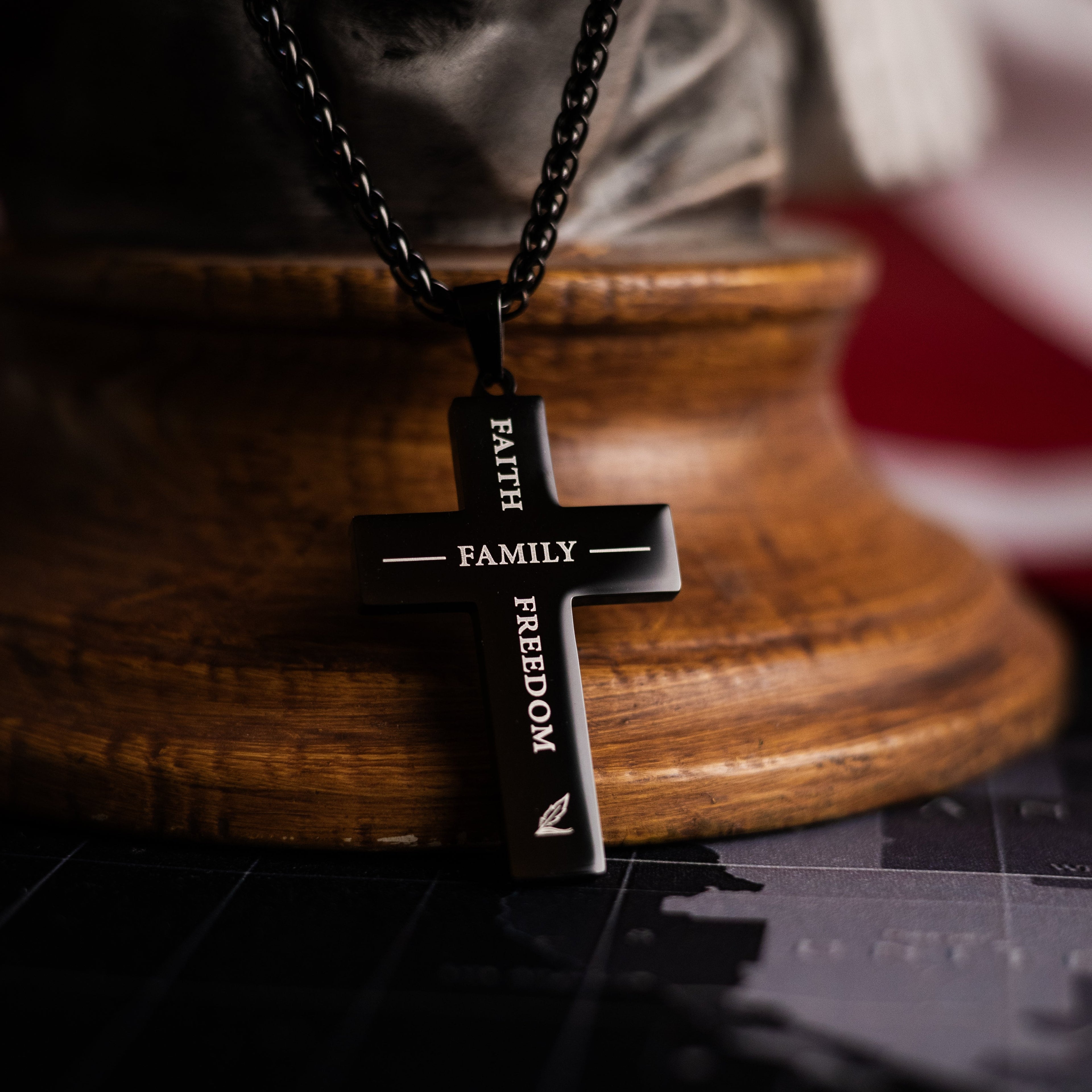 Black cross pendant with engraved words on a wooden stand with an American flag in the background